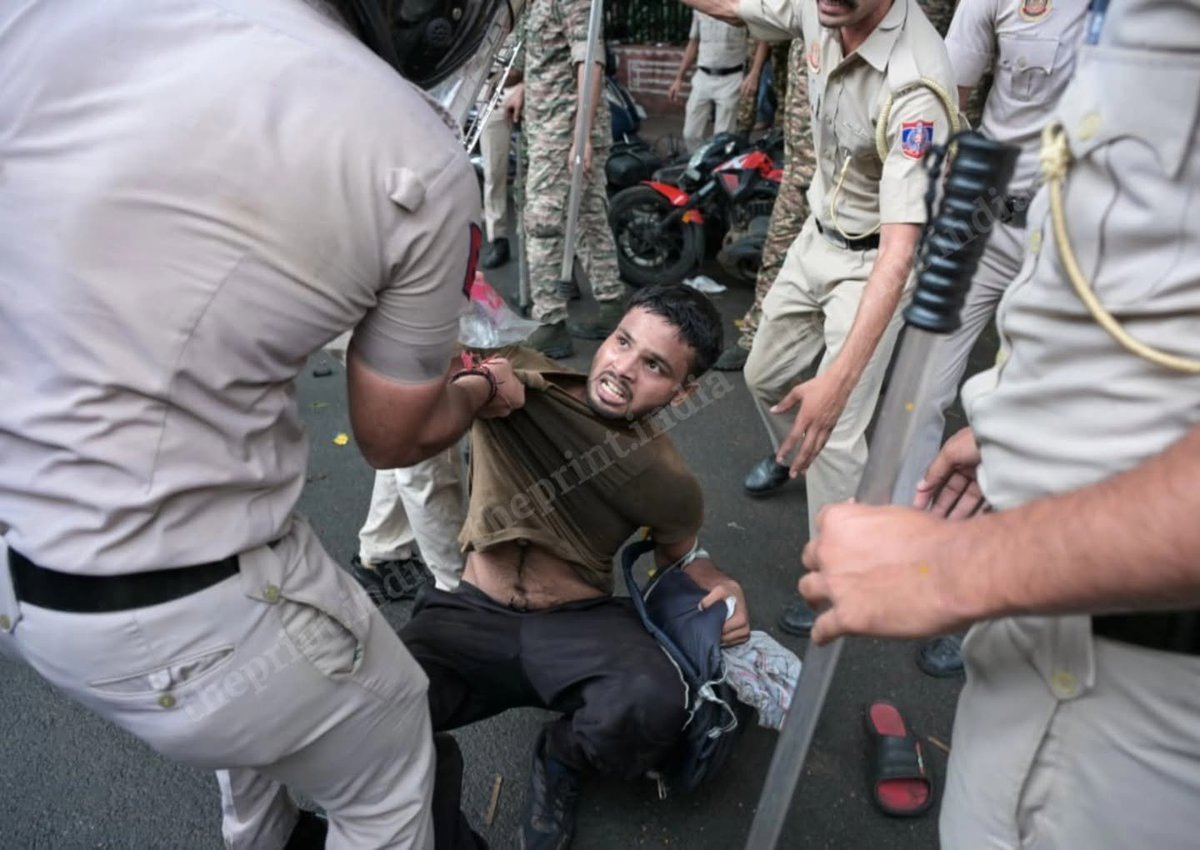 Police officers with lathis pin a young man to the road