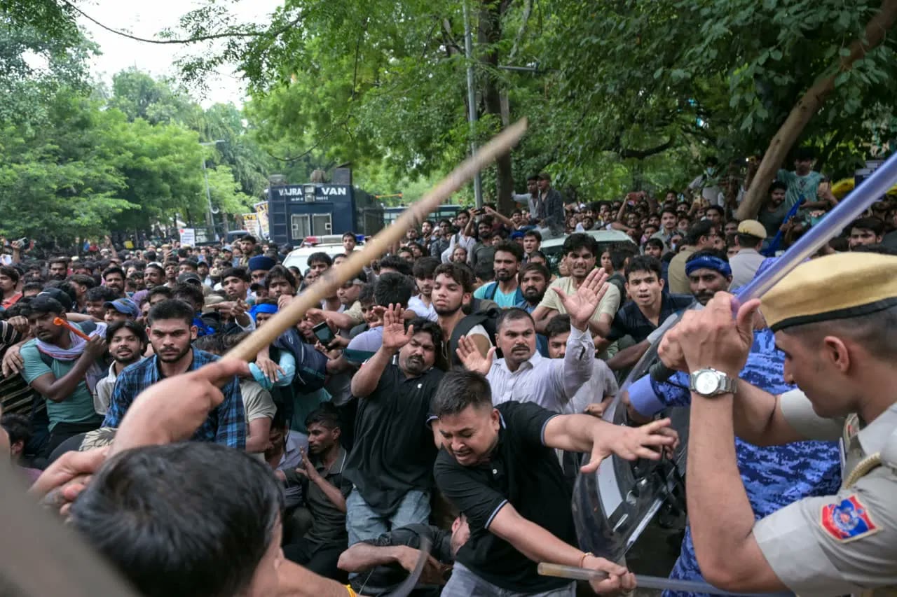 A police lathi comes down on protesters pressed against a barricade