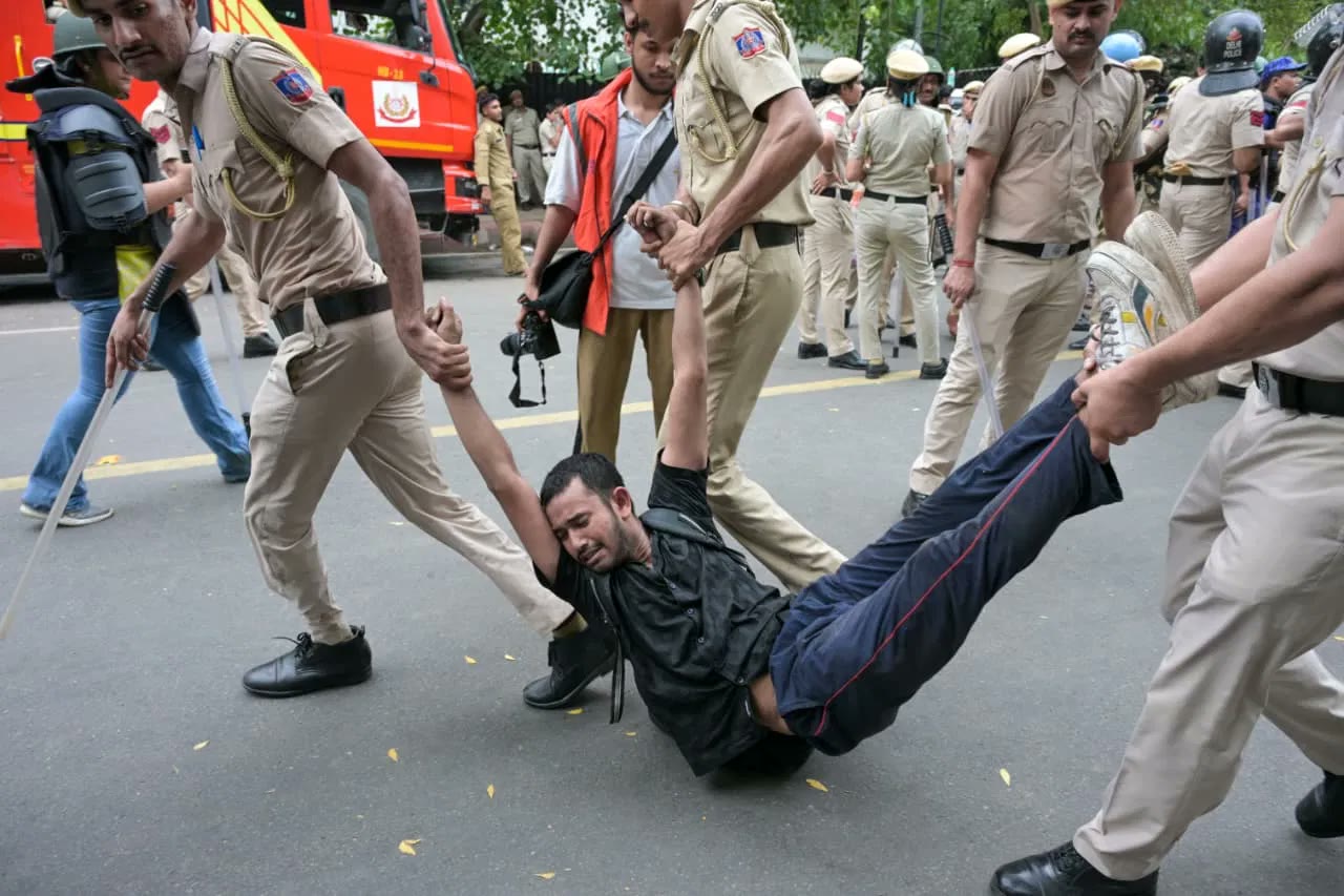 Four officers carry a protester off by his arms and legs